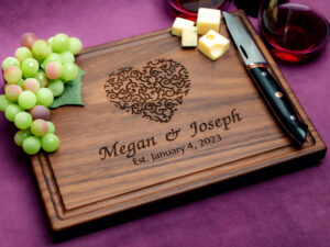 Walnut charcuterie board with green grapes two glasses of red wine and a cheese knife