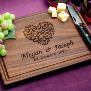 Walnut charcuterie board with green grapes two glasses of red wine and a cheese knife