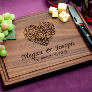 Walnut charcuterie board with green grapes two glasses of red wine and a cheese knife