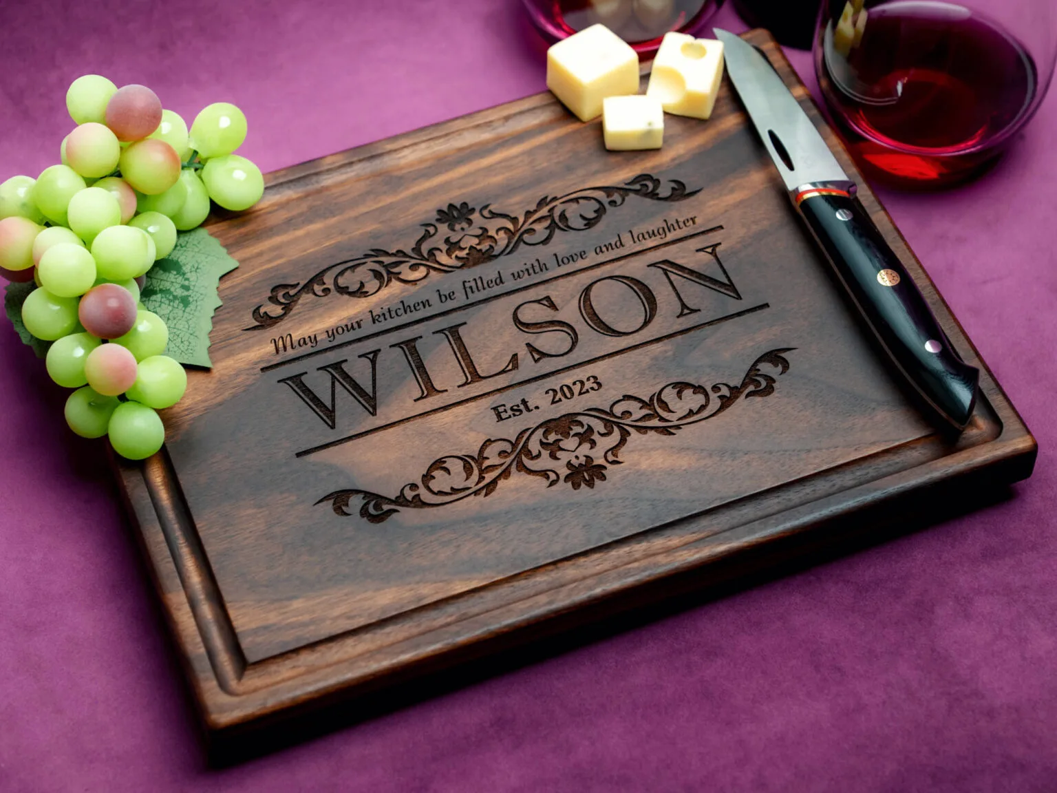 walnut charcuterie board with cheeses green grapes cheese knife and glass of red wine on purple background