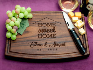 engraved walnut cutting board with housewarming theme on purple background