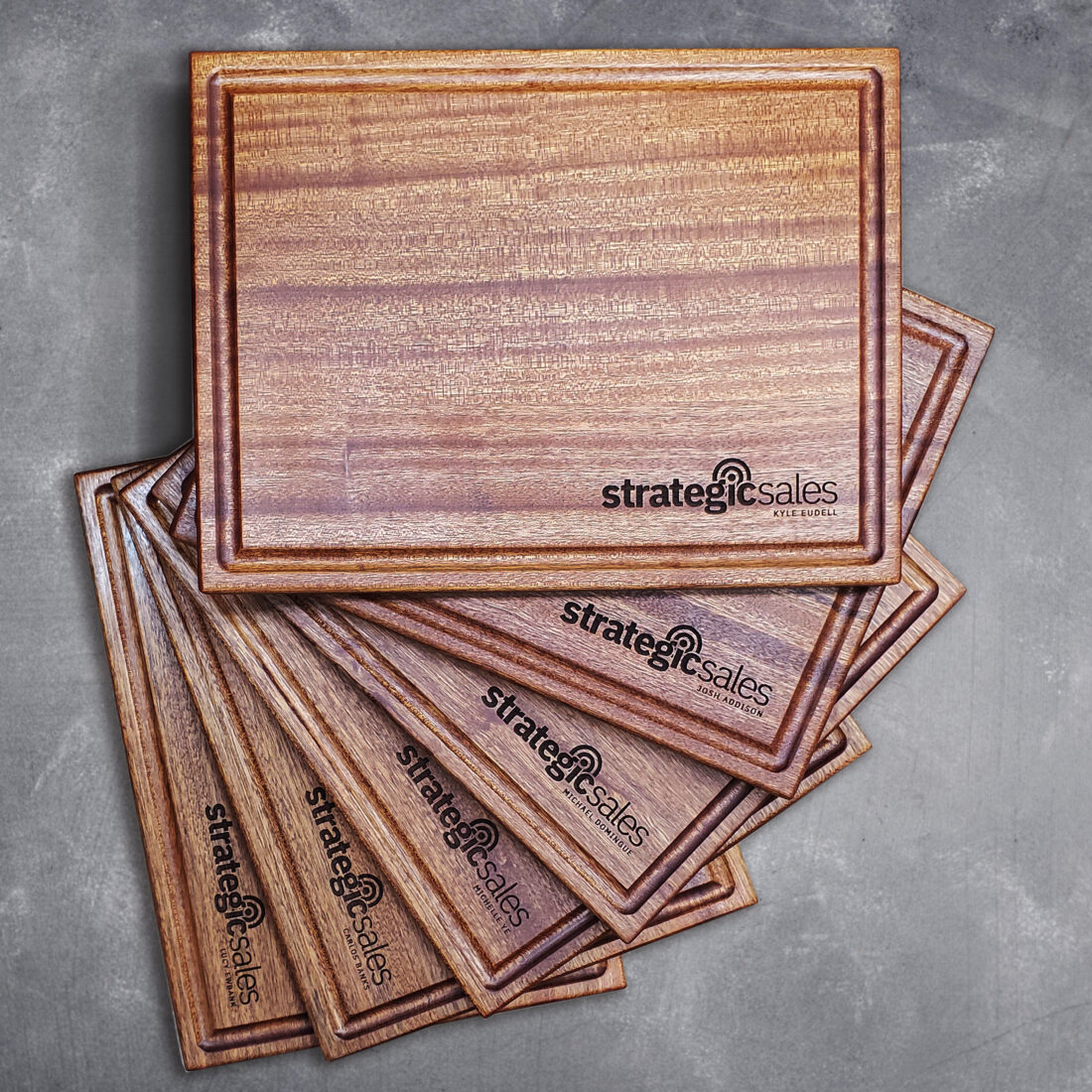 Stack of mahogany personlaized cutting boards, each with unique, individual engravings. These boards are showcased as examples of personalized corporate gifts for employee appreciation, highlighting their elegance and durability