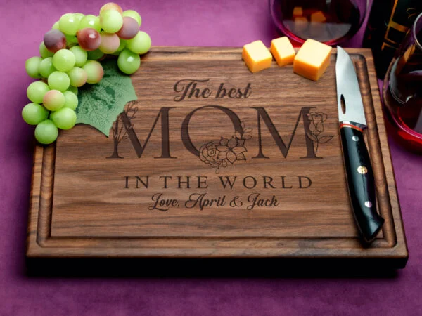 Custom walnut cutting board featuring a juice groove and engraved with the heartfelt message 'The best mom in the world'. The dark wood grain enhances the elegant look, showcasing skilled craftsmanship and thoughtful design for a perfect Mother's Day gift.