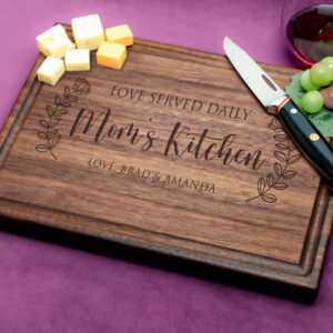 A walnut cutting board with a juice groove, elegantly engraved with 'Mom's Kitchen'. Highlighting durable wood craftsmanship, this personalized piece combines practicality and sentimentality for a perfect kitchen accessory.