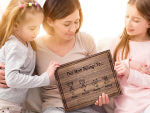 Two daughters joyfully present their mother with a personalized walnut cutting board featuring a family members design and customized engraving. The board includes a practical juice groove, making it a heartfelt and functional Mother's Day gift.