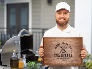 Smiling man holding engraved cutting board with barbecue background