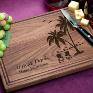 engraved wooden cutting board with tropical beach design surrounded by grapes cheese and a knife on a purple background